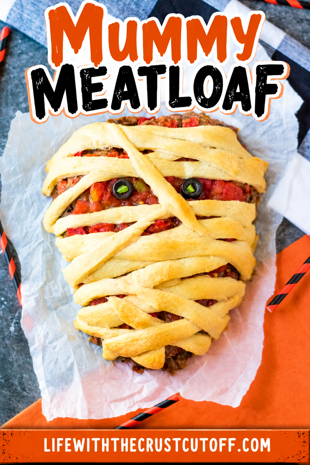 Mummy Meatloaf wrapped in golden crescent roll strips with a tomato topping and black olive eyes for Halloween.