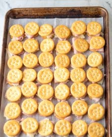 Ritz crackers laid out on a baking sheet with swiss cheese and ham and crackers on top.