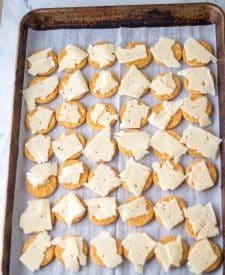 Ritz crackers laid out on a baking sheet with swiss cheese on top.