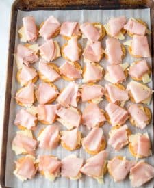 Ritz crackers laid out on a baking sheet with swiss cheese and ham on top.