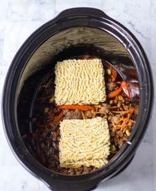 Slow Cooker Beef Ramen ingredients in slow cooker cooked with raw ramen noodles on top