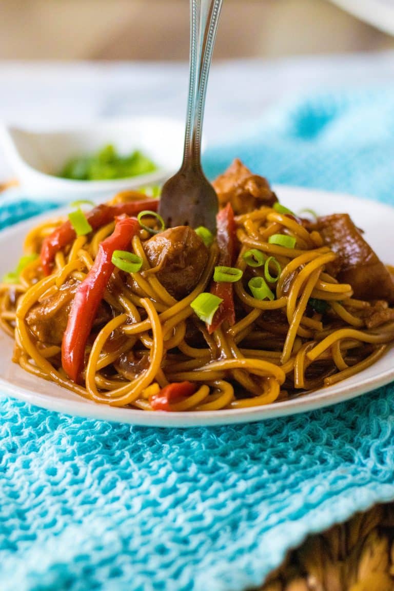 Honey garlic chicken noodles and piled on a plate with a fork in the middle