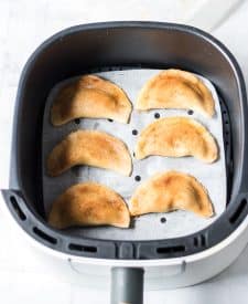 Filled empanadas brushed with butter and cinnamon sugar in the air fryer basket