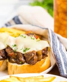 Slow Cooker Philly Cheesesteak Bites close up on a plate with melty cheese and fries