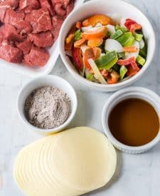 Slow Cooker Philly Cheesesteak Bites ingredient shot, peppers and onions, provolone chees,e beef broth, au jus and stew beef