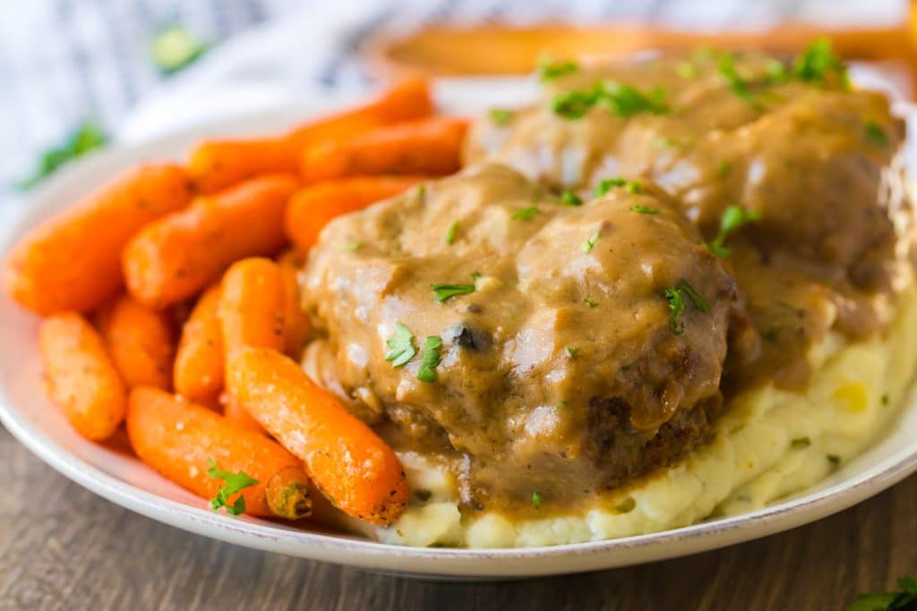 Slow Cooker Smothered Hamburgers cooked in slow cooker garnished with parsley plated with mashed potatoes and roasted carrots