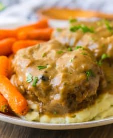 Slow Cooker Smothered Hamburgers cooked in slow cooker garnished with parsley plated with mashed potatoes and roasted carrots