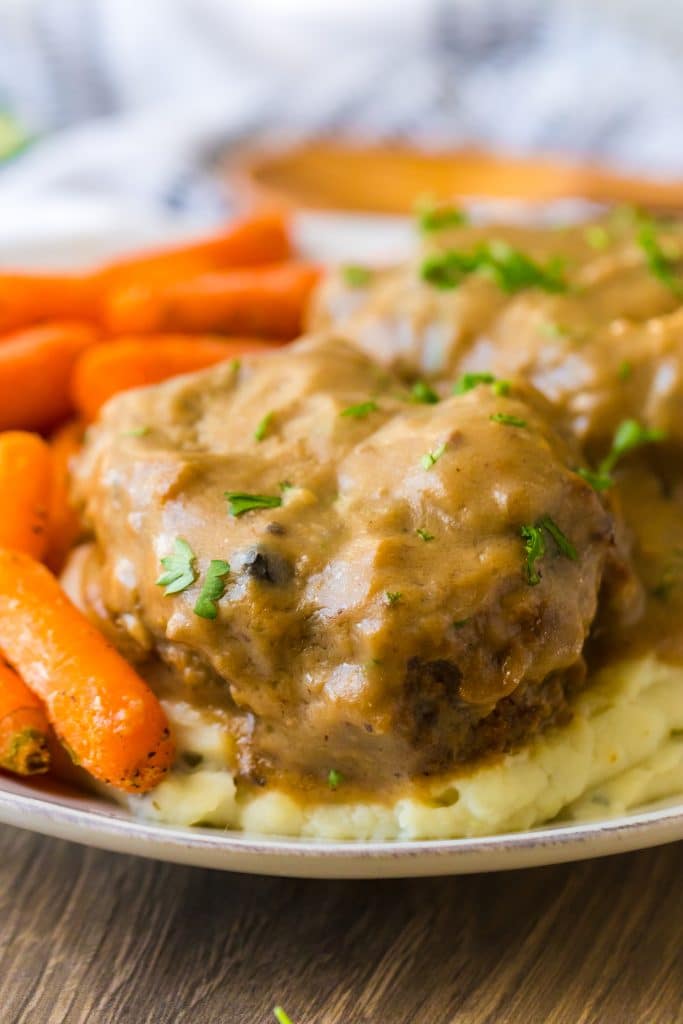 Slow Cooker Smothered Hamburgers cooked in slow cooker garnished with parsley plated with mashed potatoes and roasted carrots