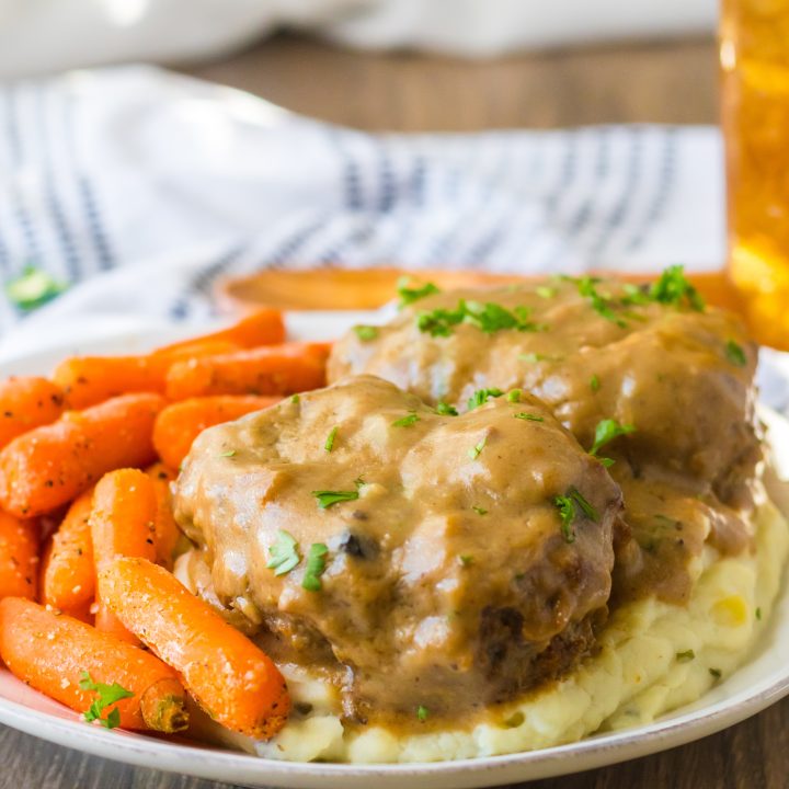 Slow Cooker Smothered Hamburgers cooked in slow cooker garnished with parsley plated with mashed potatoes and roasted carrots
