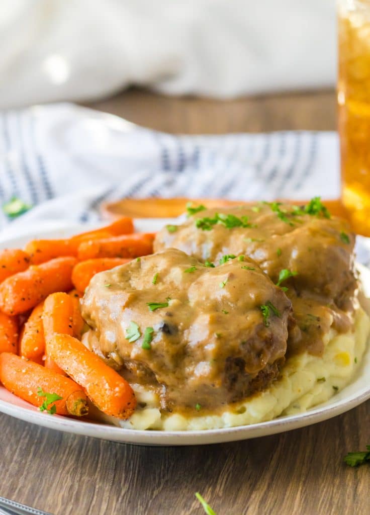 Slow Cooker Smothered Hamburgers cooked in slow cooker garnished with parsley plated with mashed potatoes and roasted carrots