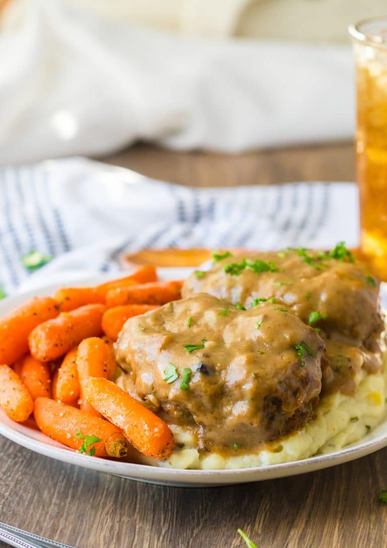 Slow Cooker Smothered Hamburgers cooked in slow cooker garnished with parsley plated with mashed potatoes and roasted carrots