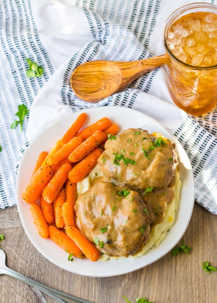 Slow Cooker Smothered Hamburgers cooked in slow cooker garnished with parsley plated with mashed potatoes and roasted carrots