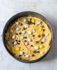Easter Cookie Cake dough in springfrom pan with chocolate chips and cadbury eggs on top