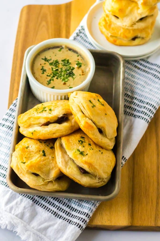 French Dip Biscuits piled in tray one a board with au jus for dipping