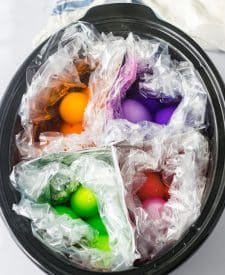 Slow Cooker Dyed Easter Eggs slow cooker shot with aluminum foil dividing the slow cooker into 4 sections, each section has a slow cooker liner and eggs and water