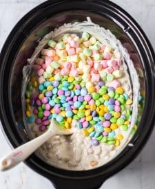 Mini marshmallows and M&Ms being stirred into slow cooker