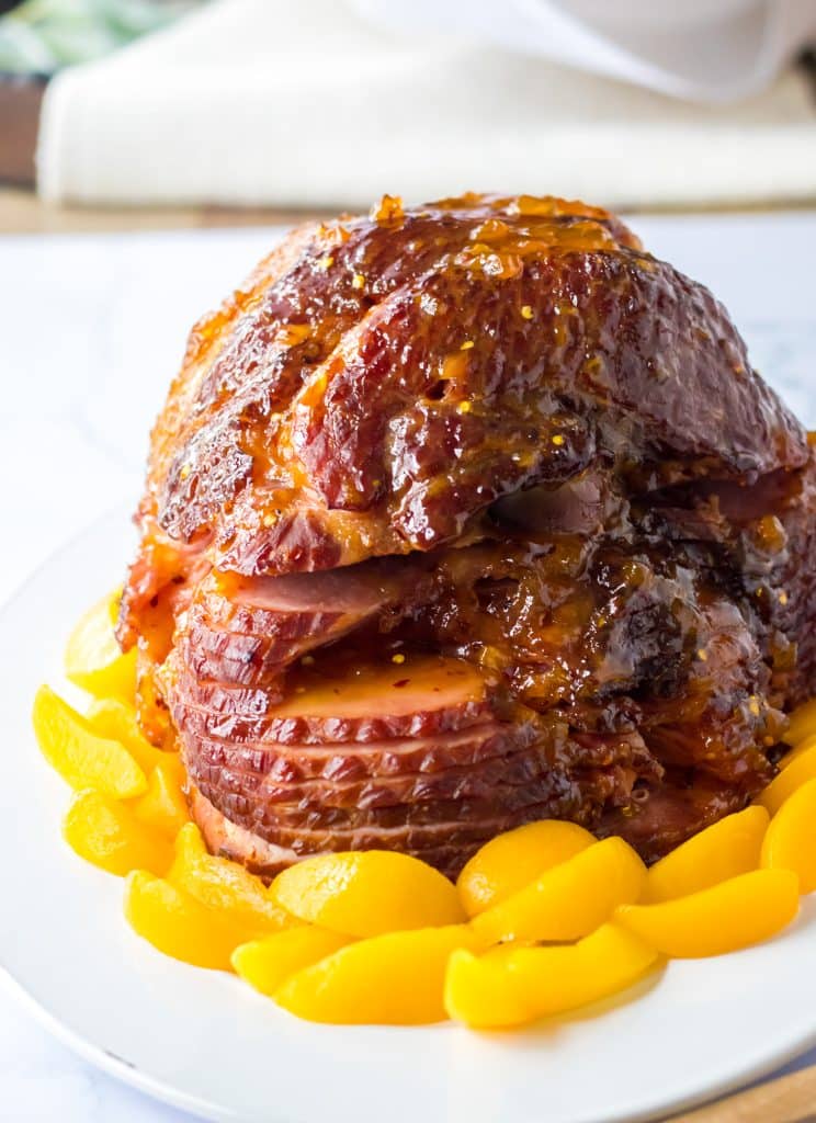 Close up shot of Slow Cooker Hot Honey Peach Glazed Ham on a plate surrounded by peaches