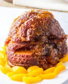 Close up shot of Slow Cooker Hot Honey Peach Glazed Ham on a plate surrounded by peaches