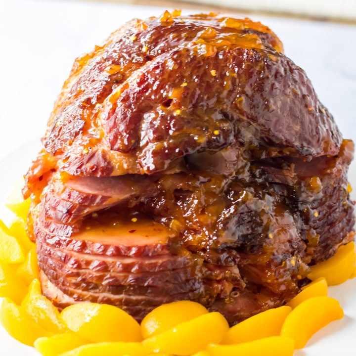 Close up shot of Slow Cooker Hot Honey Peach Glazed Ham on a plate surrounded by peaches