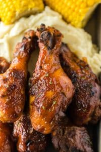Slow Cooker Honey BBQ Drumsticks piled on a plate with mashed potatoes and corn