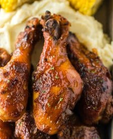 Slow Cooker Honey BBQ Drumsticks piled on a plate with mashed potatoes and corn
