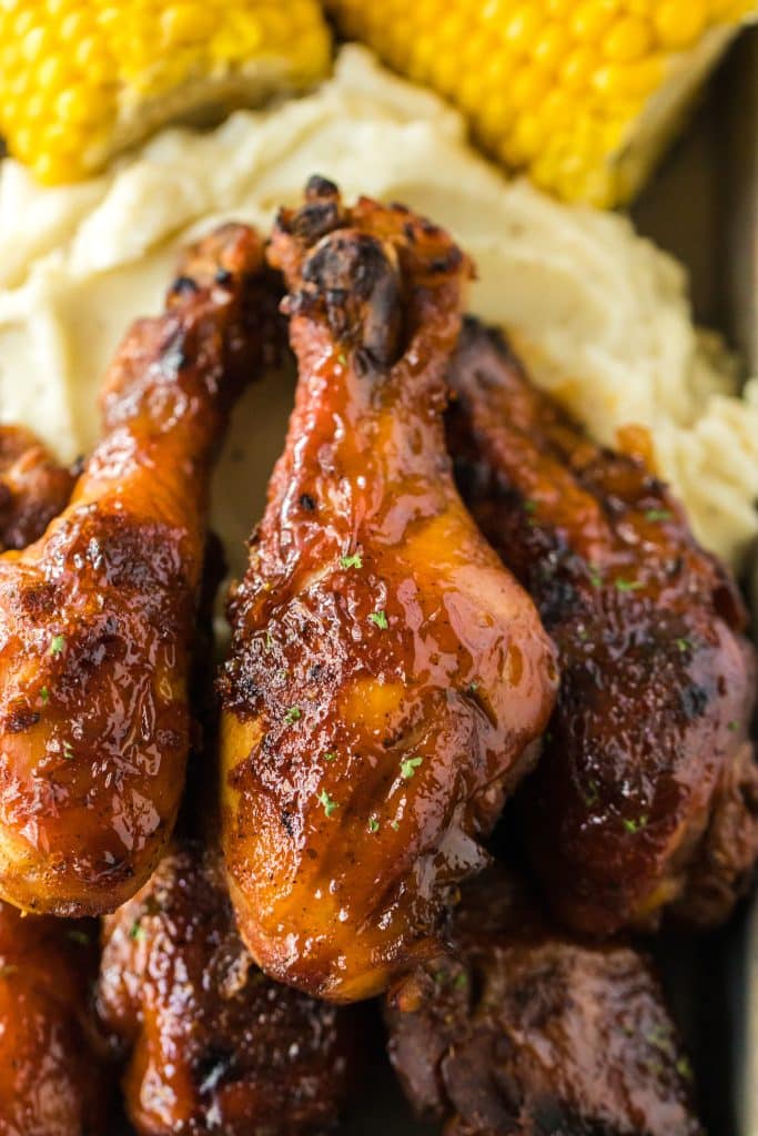 Slow Cooker Honey BBQ Drumsticks piled on a plate with mashed potatoes and corn