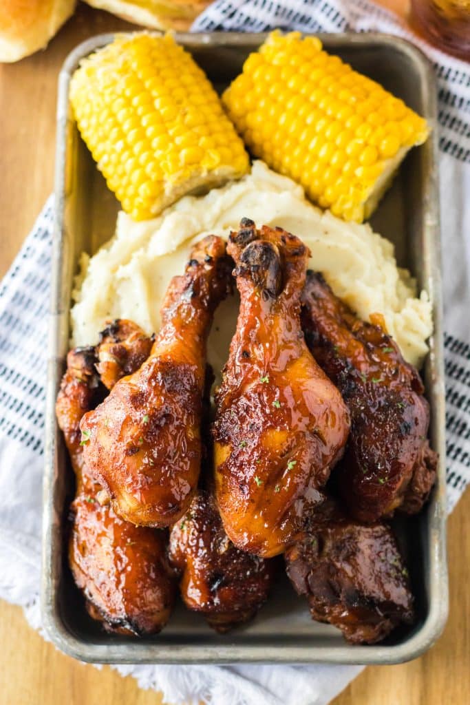 Slow Cooker Honey BBQ Drumsticks piled on a plate with mashed potatoes and corn