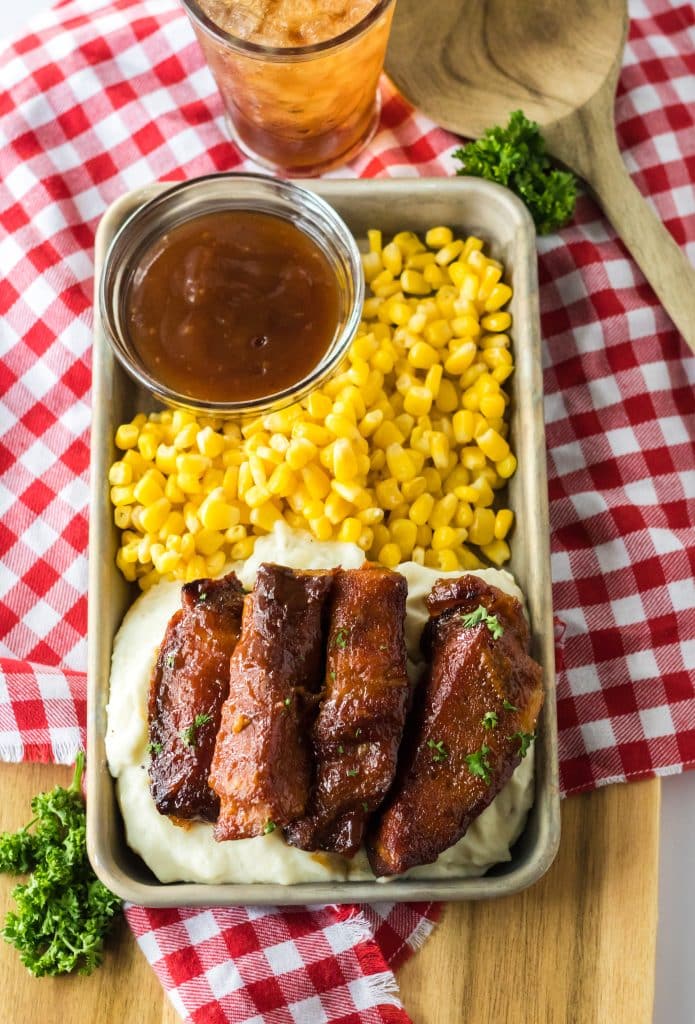 Slow Cooker Honey Peach Country Ribs piled on a plate with mashed potatoes and corn