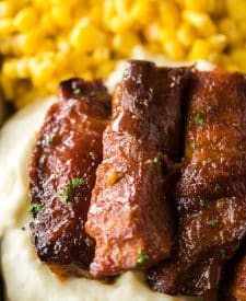 Slow Cooker Honey Peach Country Ribs piled on a plate with mashed potatoes and corn