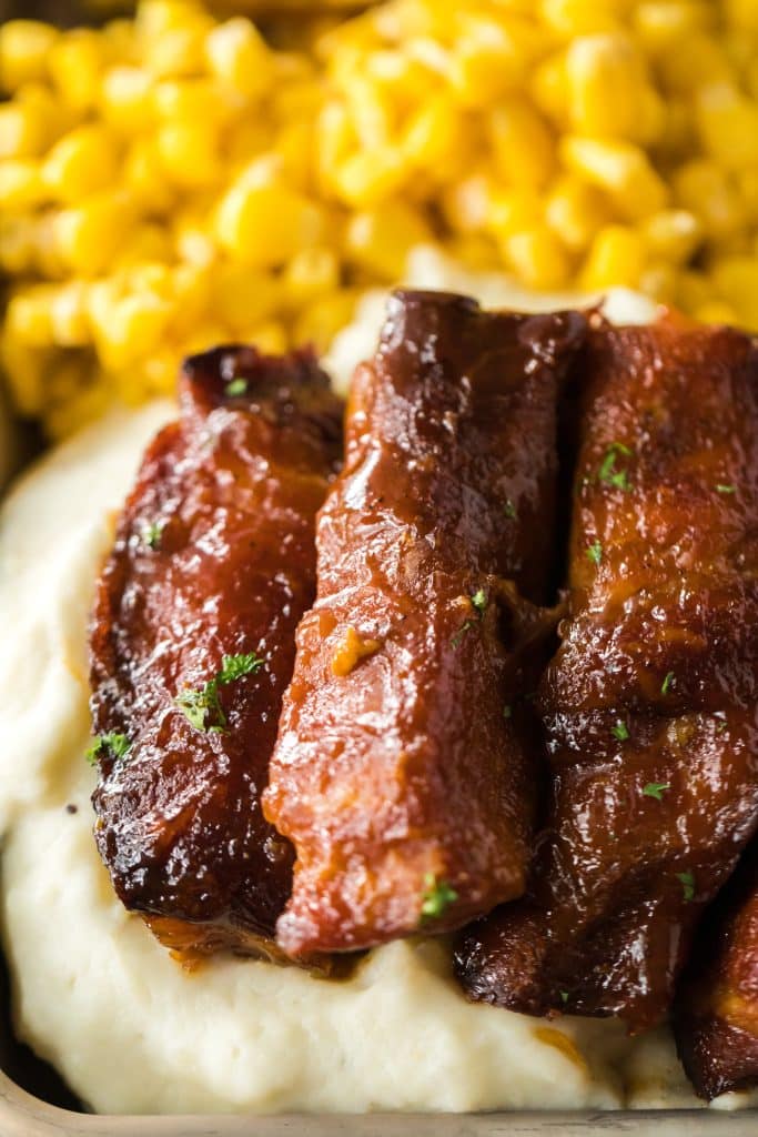 Slow Cooker Honey Peach Country Ribs piled on a plate with mashed potatoes and corn