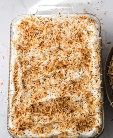 Pina Colada Cheesecake Bars in pan with whipped topping and toasted coconut