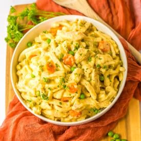 Creamy slow cooker chicken and noodles in a bowl with peas and carrots