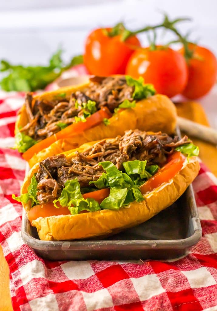 Slow cooker roast beef po’ boy sandwich with tender beef, gravy, lettuce, and pickles on a French bread roll.