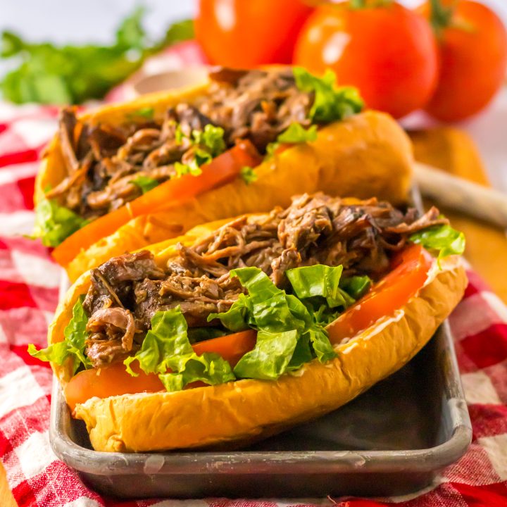 Slow cooker roast beef po’ boy sandwich with tender beef, gravy, lettuce, and pickles on a French bread roll.