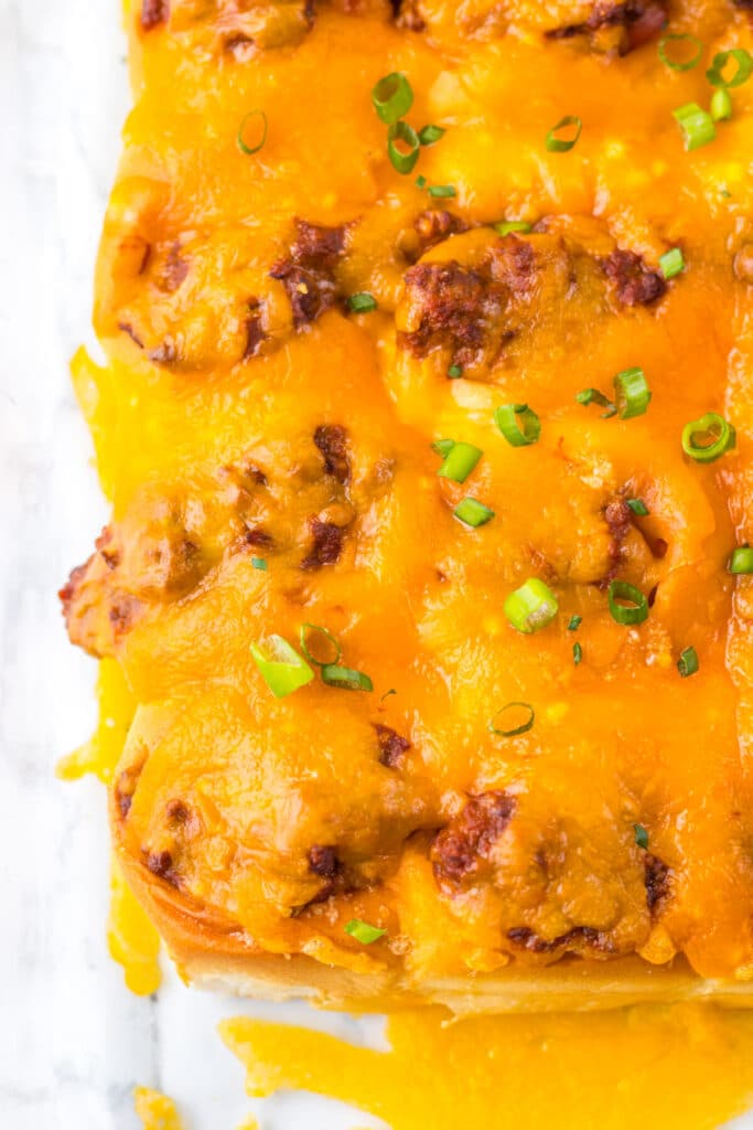 Mini chili cheese dog sliders baked on Hawaiian rolls with hot dogs, chili, melted cheddar cheese, and toppings, perfect for an easy weeknight dinner or game day appetizer.