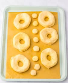 Uncooked biscuit dough cut into doughnut shapes on white surface with cider and sugar