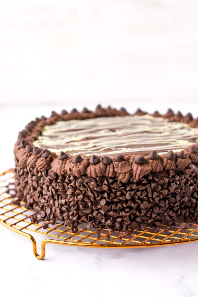 "Rich four-layer chocolate mousse cake topped with ganache and white chocolate drizzle, served on a cake stand."