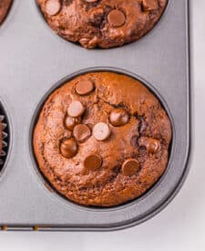 Jumbo Costco-style double chocolate muffins with melty chocolate chips on top, baked at home and cooling in liners on a wire rack.