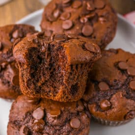 Jumbo Costco-style double chocolate muffins with melty chocolate chips on top, baked at home and cooling in liners on a wire rack.