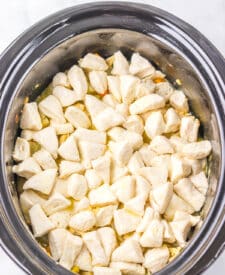 Overhead shot of raw biscuit dough on top of creamy pot pie mixture in slow cooker.
