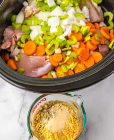 Overhead shot of slow cooker filled with chicken, carrots, and herbs