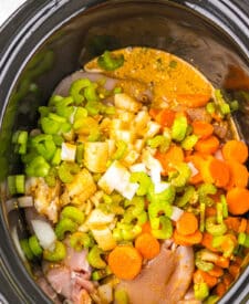 Overhead shot of slow cooker filled with chicken, carrots, and herbs