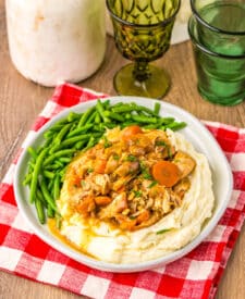 Chicken pot roast dinner with carrots, potatoes, and green beans served on a white plate