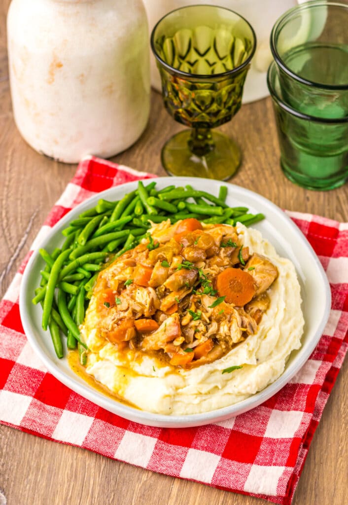 Chicken pot roast dinner with carrots, potatoes, and green beans served on a white plate