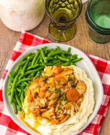 Chicken pot roast dinner with carrots, potatoes, and green beans served on a white plate