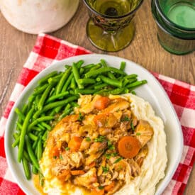 Chicken pot roast dinner with carrots, potatoes, and green beans served on a white plate