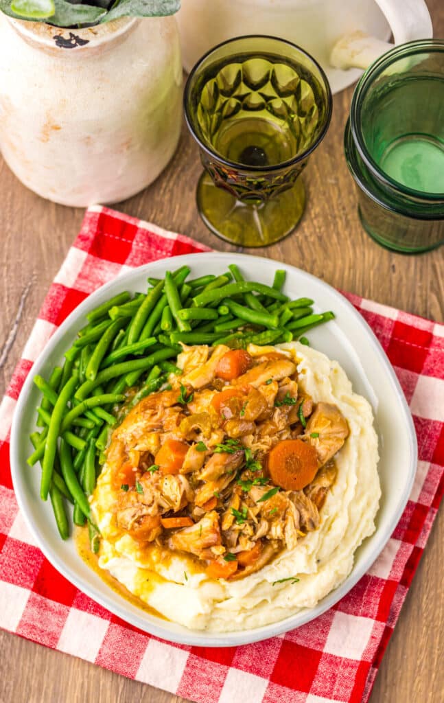 Chicken pot roast dinner with carrots, potatoes, and green beans served on a white plate