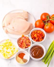 Raw ingredients for Monterey Chicken laid out on white background, including chicken, bacon, cheese, and tomatoes