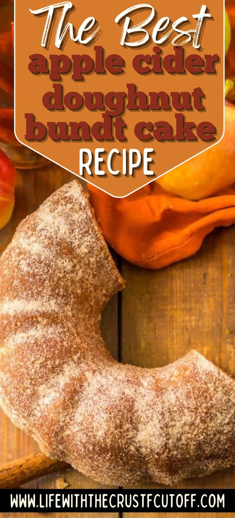 A sugared apple cider doughnut bundt cake on a rustic wooden table with apples and fall linens.