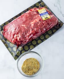 raw prime rib roast with garlic and herbs next to small bowls of seasoning